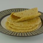 A stack of five gluten free chickpea flour wraps on a plate, the top one folded to show the thickness.