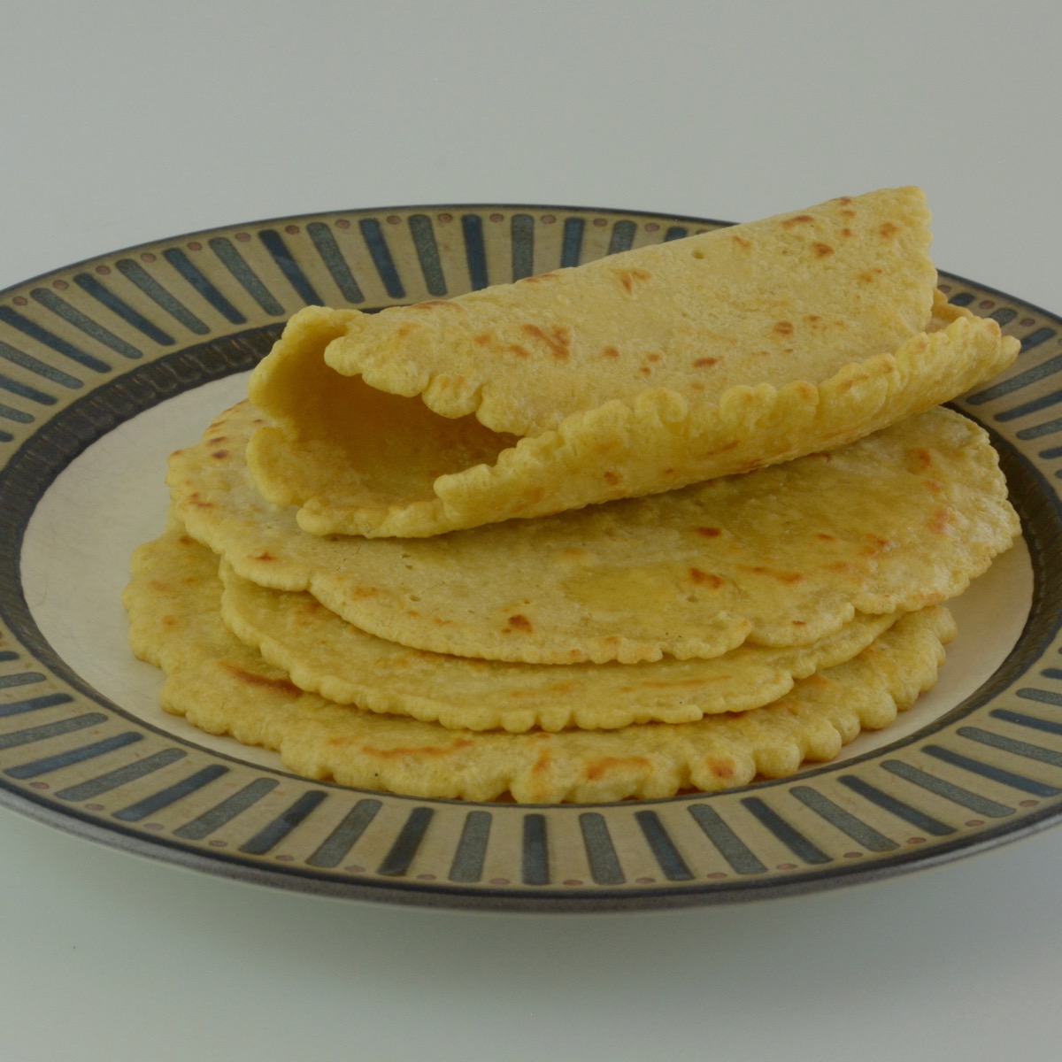 A stack of five gluten free chickpea flour wraps on a plate, the top one folded to show the thickness.