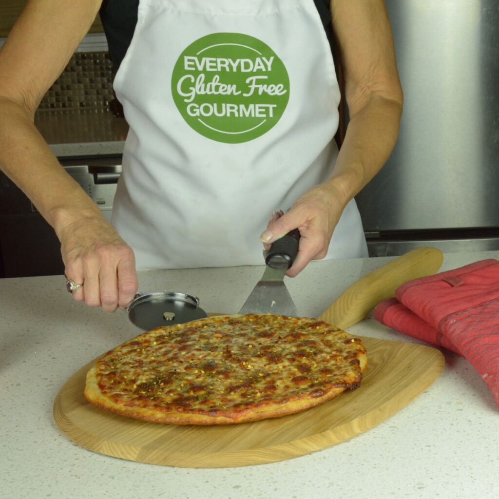 Cinde sliding a whole gluten free pizza off the pizza peel onto a wooden board.