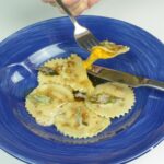 A fork picking one gluten free butternut squash ravioli out of a bowl.
