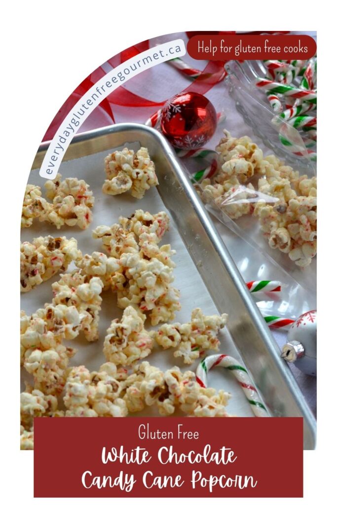A pan with clumps of White Chocolate Candy Cane Popcorn beside gift bags, candy canes and ribbon.
