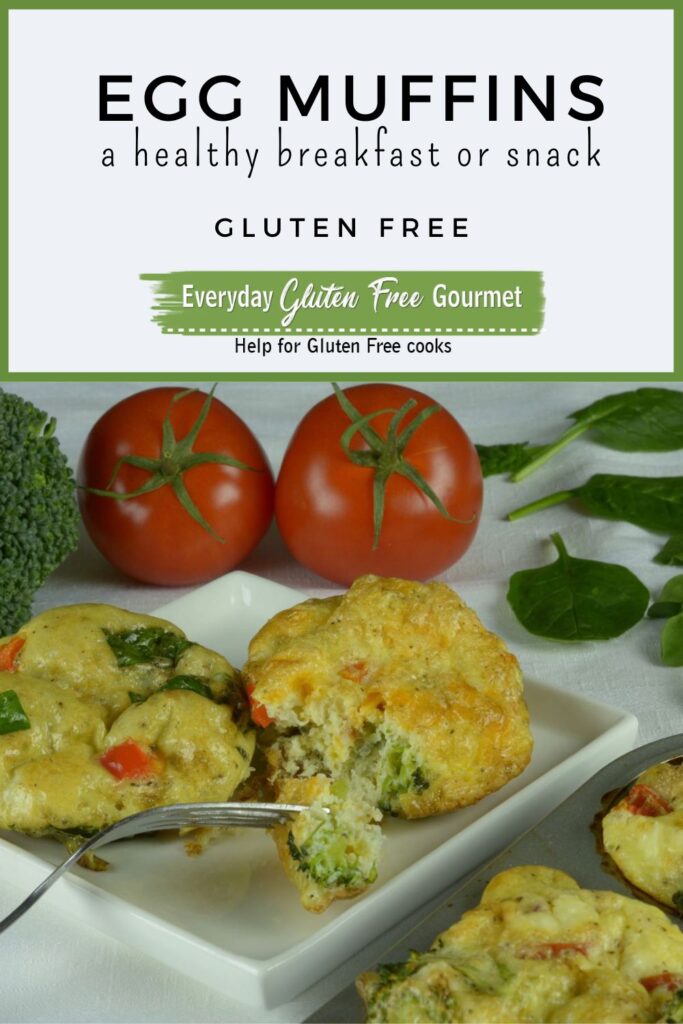 A plate with two cooked Egg Muffins surrounded by spinach, tomatoes and broccoli.