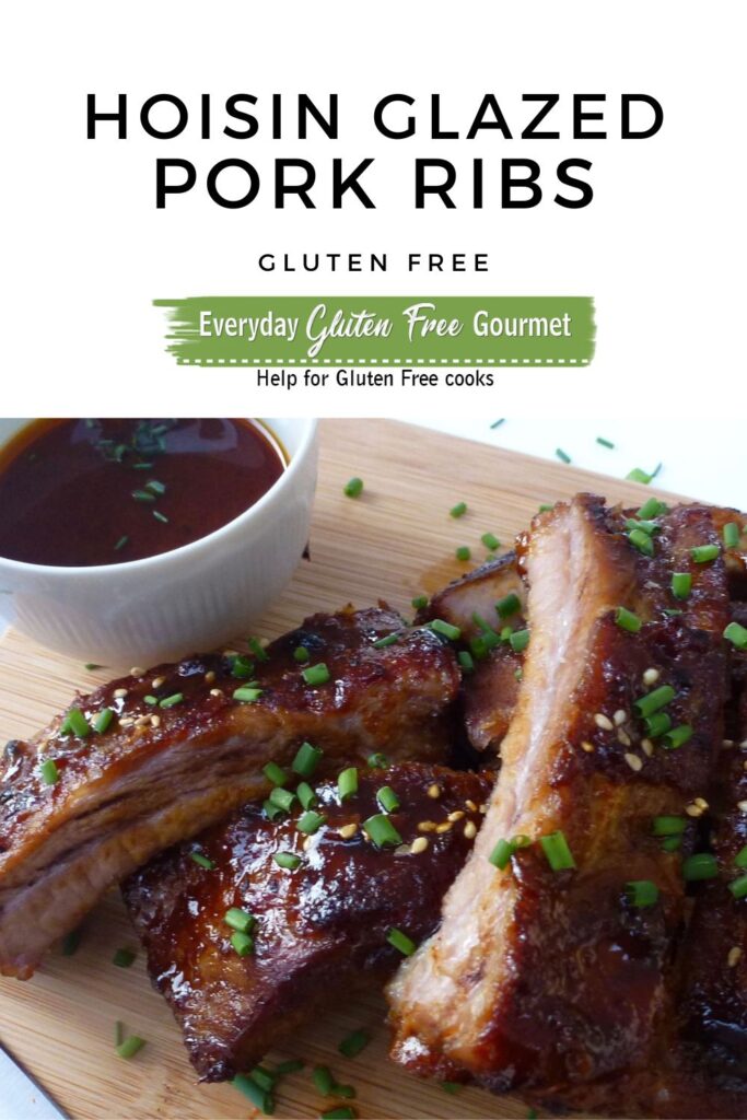 A cutting board with hoisin glazed pork ribs sprinkled with sesame seeds and chopped green onion with extra sauce on the side.