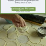 A hand holding one perogy above the counter covered in circles of dough ready to make more perogies.