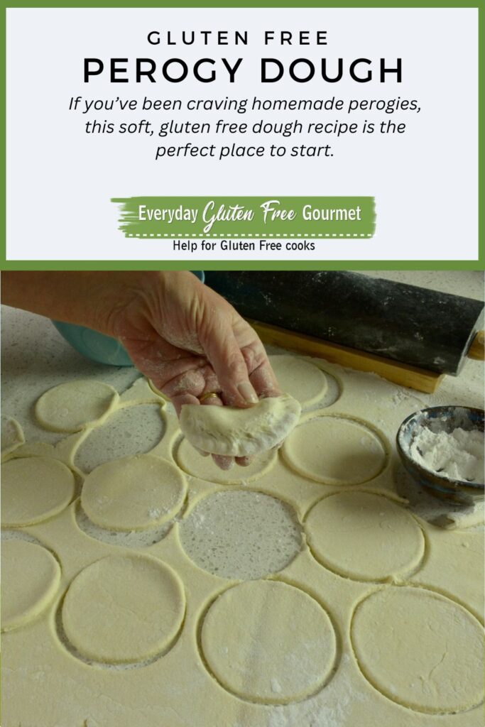 A hand holding one perogy above the counter covered in circles of dough ready to make more perogies.