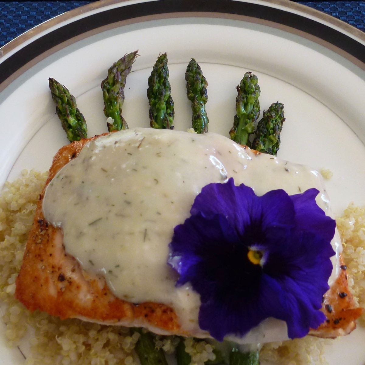 Grilled Salmon with White Barbecue Sauce on top of cooked asparagus with a purple pansy garnish.