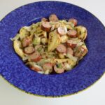 A bowl of Gluten Free Grilled Perogies with Sausage and onions, all grilled and tossed with a mustard dressing.