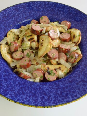 A bowl of Gluten Free Grilled Perogies with Sausage and onions, all grilled and tossed with a mustard dressing.