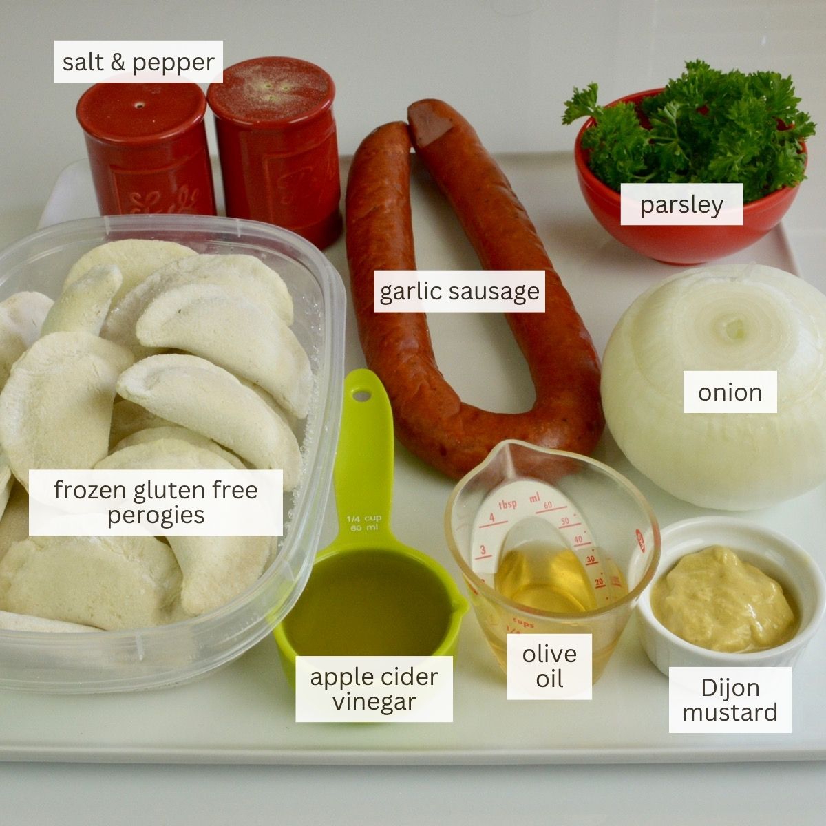 Ingredients for gluten free grilled perogies laid out on a tray: garlic sausage, frozen perogies, onion, oil, apple cider vinegar, mustard, salt and pepper.