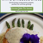 Grilled Salmon with White Barbecue Sauce on top of cooked asparagus with a purple pansy garnish.