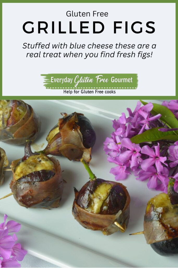 Grilled Figs Stuffed with Blue Cheese and wrapped with prosciutto on a white platter surrounded by pink flowers.