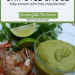 A dish of Avocado Chipotle Sauce surrounded by grilled shrimp, fresh lime wedges and cilantro.