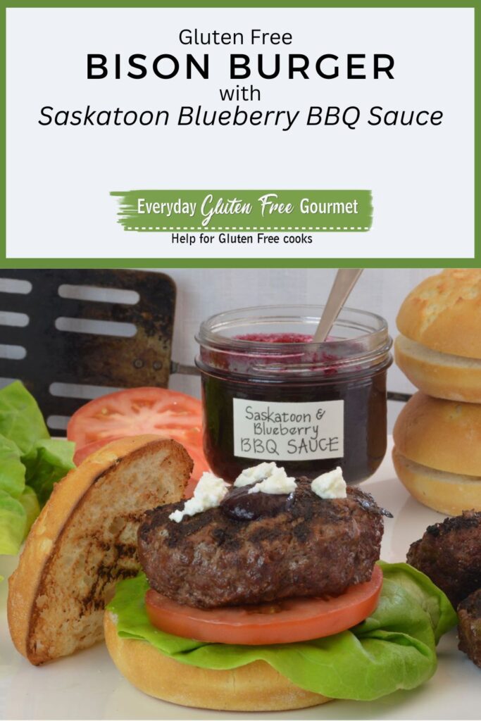 A Bison Burger on a bun with tomato, lettuce and goat cheese, with a jar of Saskatoon Blueberry Barbecue Sauce beside it.