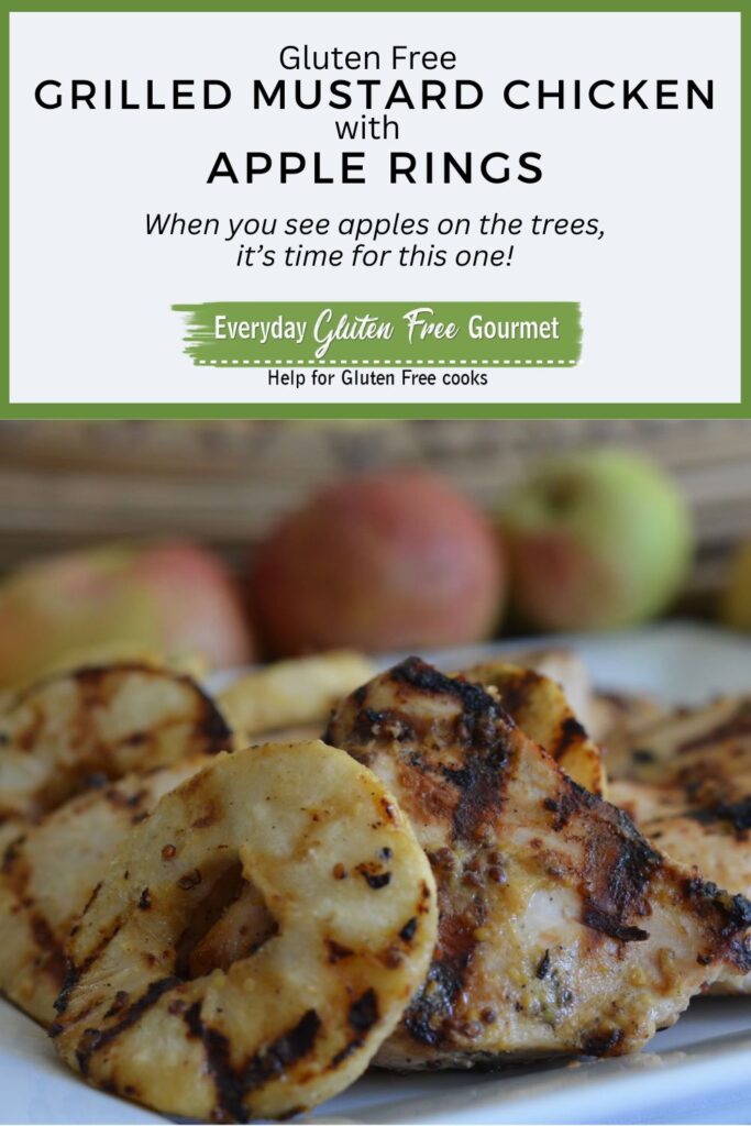 A platter of Grilled Mustard Chicken with Apple Rings in front of a row of red apples.