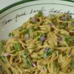 A bowl of gluten free Spicy Sesame Noodles with green beans and a sprinkling of fresh chives and the blossoms.