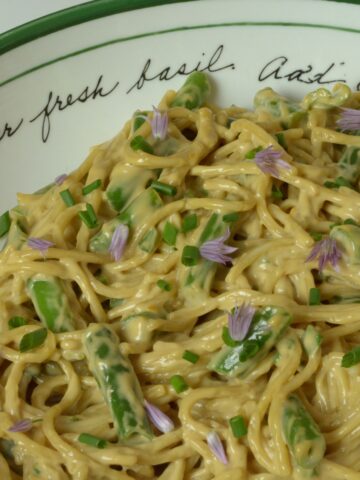 A bowl of gluten free Spicy Sesame Noodles with green beans and a sprinkling of fresh chives and the blossoms.