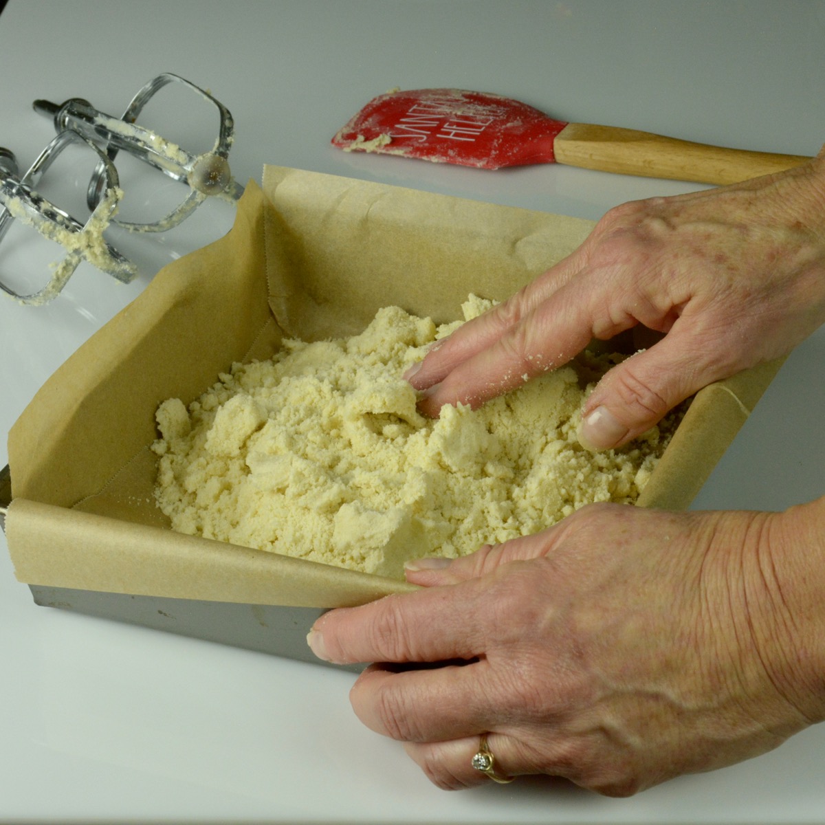 Someone pressing the crumb mixture into the bottom of a baking pan with their fingers.