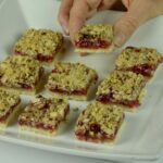 Someone taking a piece from a tray of gluten free Raspberry Crumble Bars.