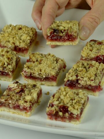 Someone taking a piece from a tray of gluten free Raspberry Crumble Bars.
