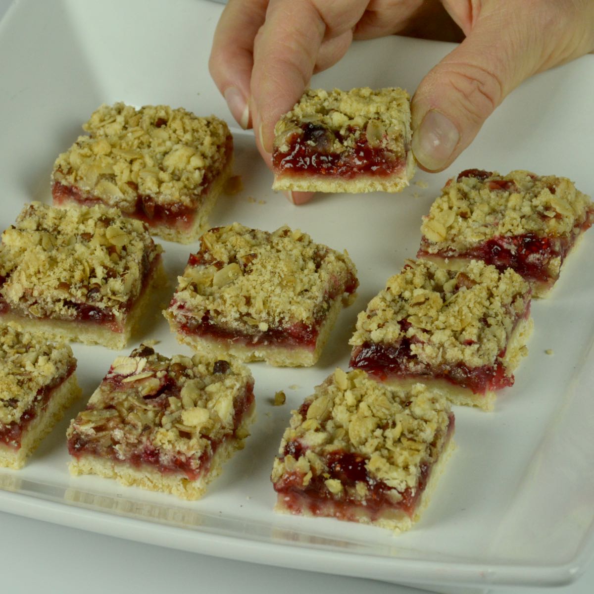Someone taking a piece from a tray of gluten free Raspberry Crumble Bars.