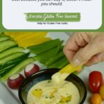 An oval shaped dish filled with lemony hummus surrounded by cherry tomatoes, cucumber and yellow pepper slices.