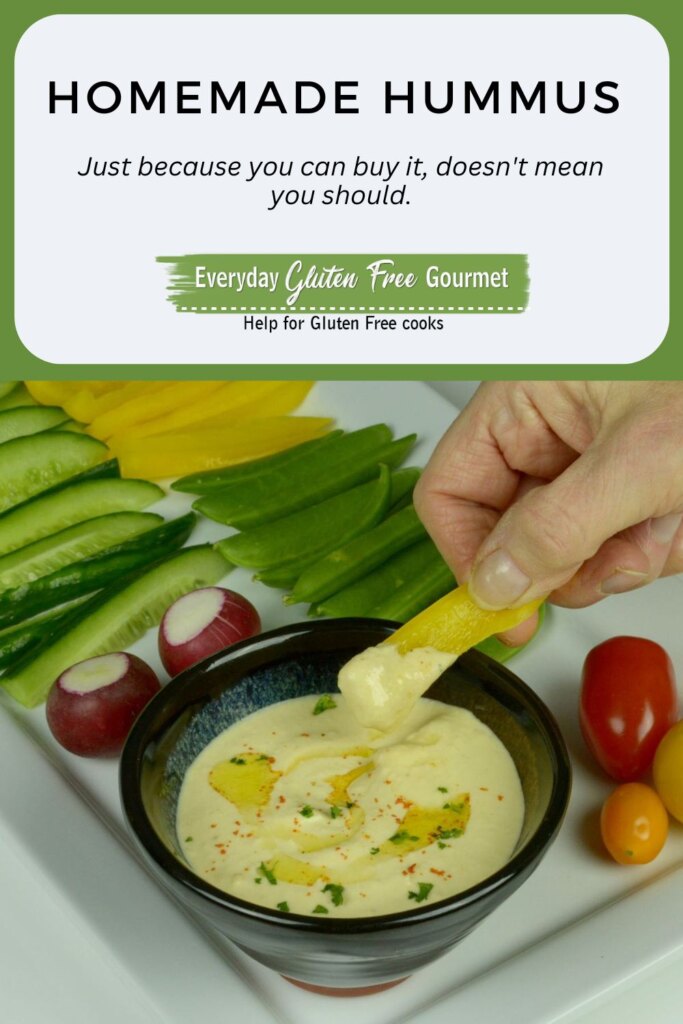 An oval shaped dish filled with lemony hummus surrounded by cherry tomatoes, cucumber and yellow pepper slices.