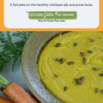 Roasted Carrot Hummus in a round dish sprinkled with toasted pumpkin seeds and surrounded by garden carrots.