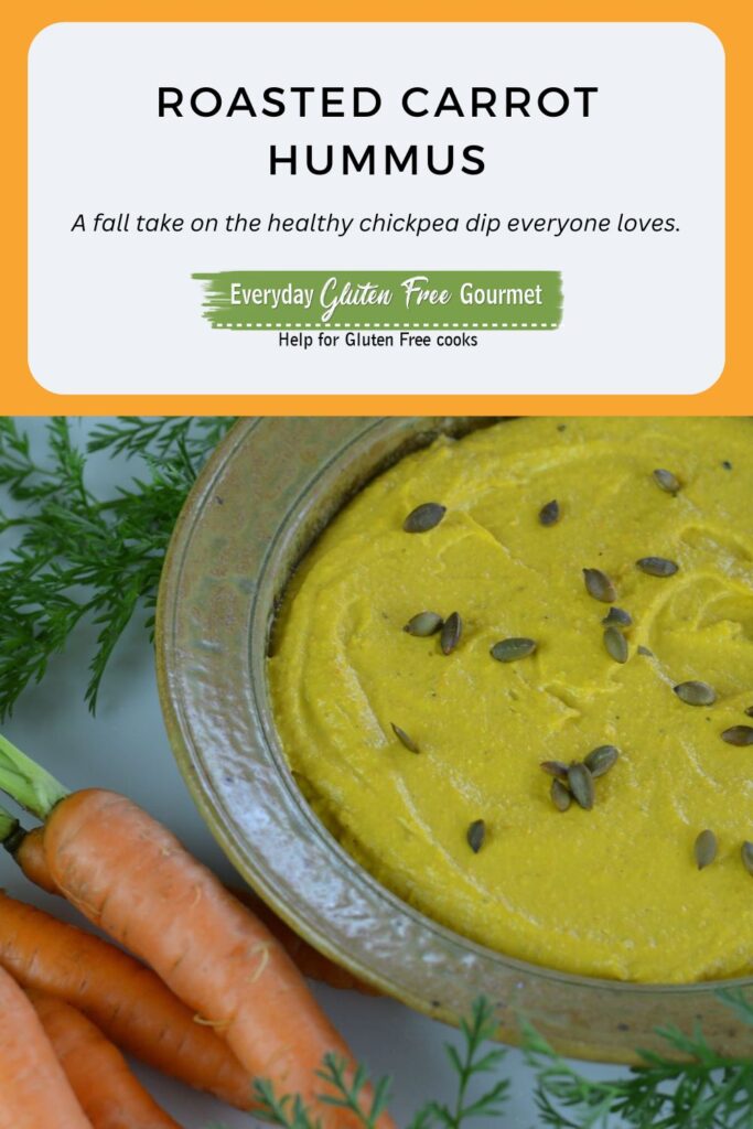 Roasted Carrot Hummus in a round dish sprinkled with toasted pumpkin seeds and surrounded by garden carrots.