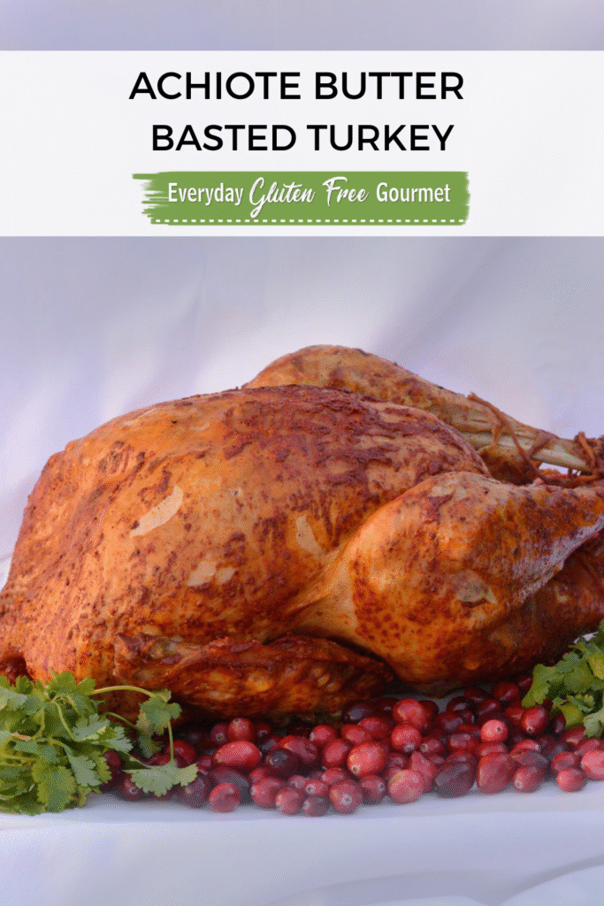 A whole Achiote Butter Basted Turkey on a platter surrounded by cranberries and cilantro.