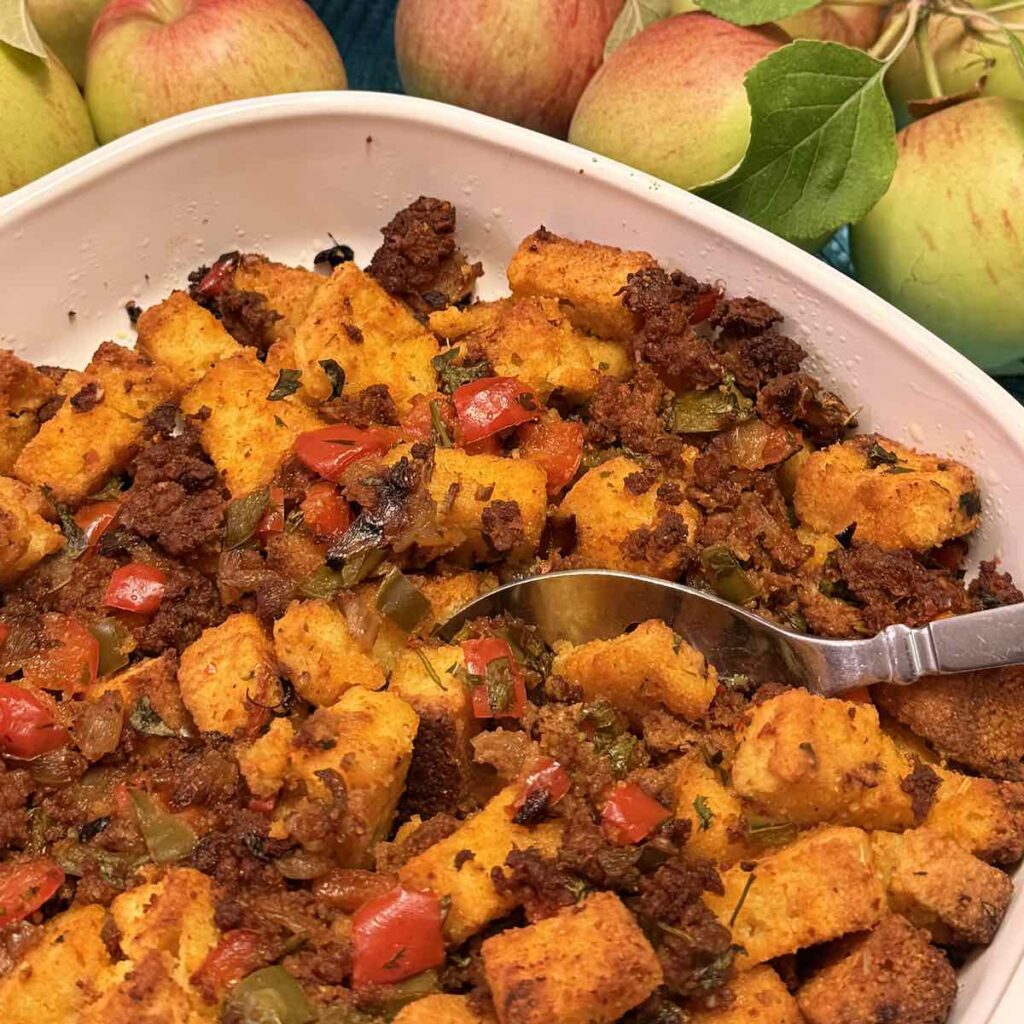 A casserole dish of gluten free Cornbread Chorizo Stuffing surrounded by apples.