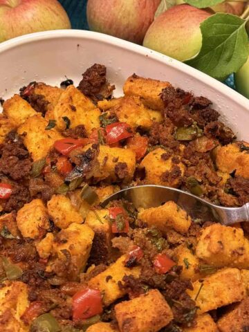 A casserole dish of gluten free Cornbread Chorizo Stuffing surrounded by apples.