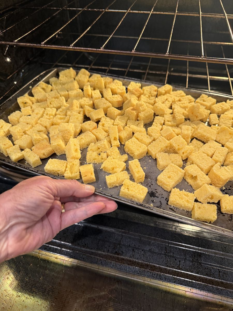 Someone sliding a baking sheet covered in cubes of gluten free cornbread into the oven.