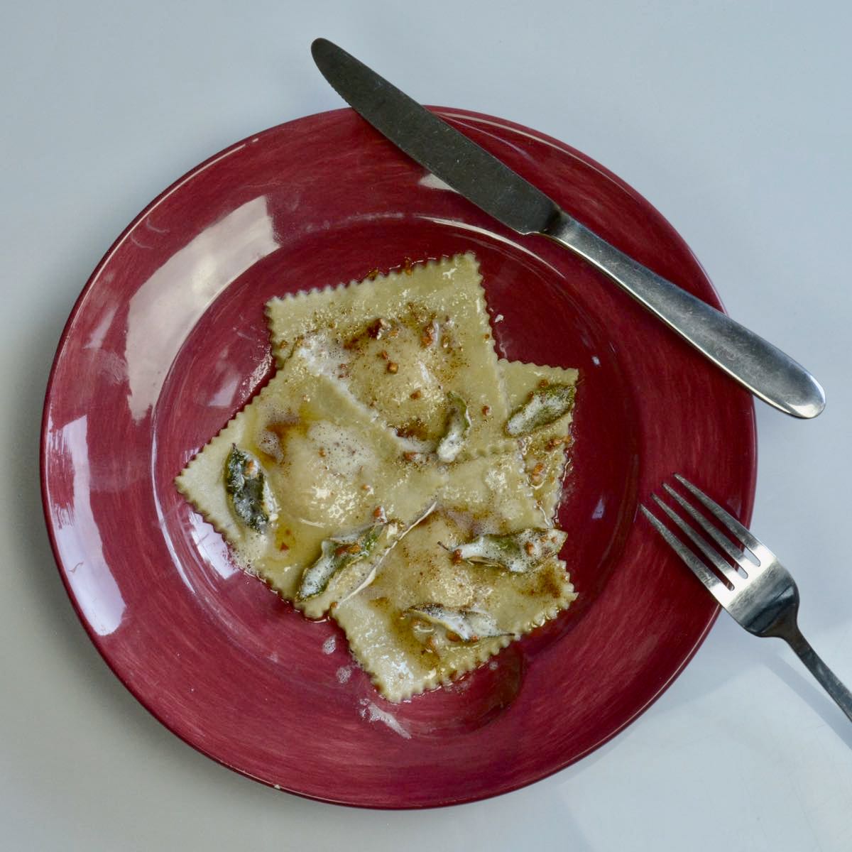 A bowl of gluten free butternut squash ravioli with a knife and fork beside it.