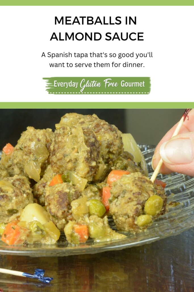 A plate of Spanish Meatballs in Almond Sauce with a hand grabbing one with a toothpick.