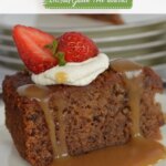 A piece of Gluten Free Sticky Date Pudding on a plate with caramel sauce dripping down the sides topped with whipped cream and a strawberry.