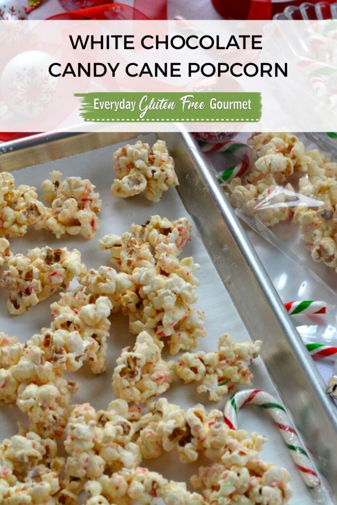 A pan with clumps of White Chocolate Candy Cane Popcorn beside gift bags, candy canes and ribbon.