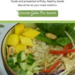 A bowl filled with brown rice, cucumber, spinach, cabbage slaw, mango and roasted peanuts; with peanut dressing on the side.