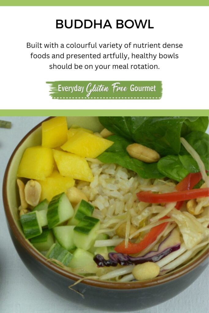 A bowl filled with brown rice, cucumber, spinach, cabbage slaw, mango and roasted peanuts; with peanut dressing on the side.