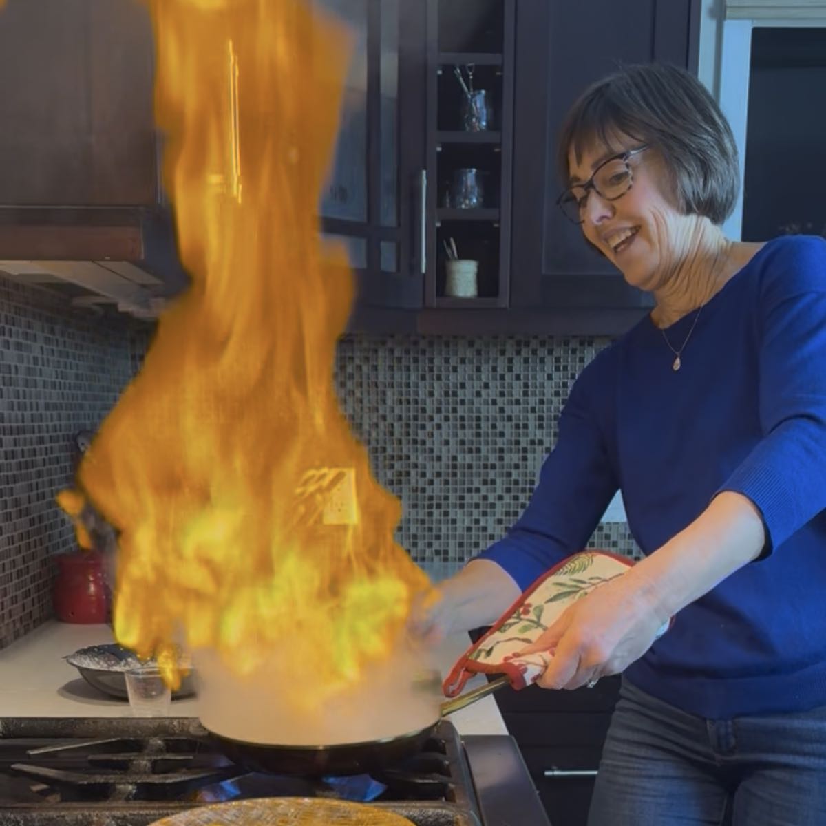 Cinde holding a flaming frying pan just after adding brandy to saganaki.
